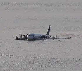 Un avion blanc, celui du vol 1549 d'US Airways, posé sur la rivière Hudson à New York. Des passagers sont sur les toboggans et les ailes de l'appareil.