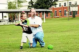  Un jeune garçon avec une batte de base-ball, son père assis à ses côtés modifie son geste