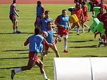 Des joueurs de rugby en chasubles avec du matériel d'entraînement sur un terrain.