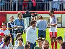 Un joueur de rugby parlant devant un homme portant une caméra, entouré par l'équipe technique et une présentatrice.
