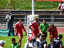 Des joueurs et des arbitres de rugby sont rassemblés autour d'une zone d'en-but, devant une caméra fixe.