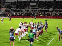 Des joueurs de rugby forment deux lignes, un autre tient un ballon au-dessus de sa tête.