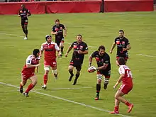 Des joueurs de rugby courent en ligne, d'autres se dirigent vers celui portant le ballon.