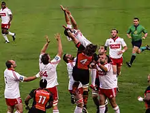 Les joueurs de deux équipes sautent afin de récupérer la retombée d'un ballon de rugby.