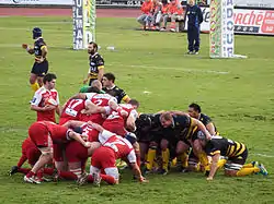 Des joueurs de rugby forment deux regroupements pour préparer une mêlée, deux autres se tiennent à proximité.