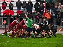 Des joueurs de rugby forment une mêlée qui vient de s'écrouler, un arbitre à proximité lève le bras.