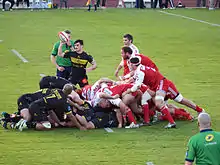 Des joueurs de rugby forment une mêlée qui vient de s'écrouler, un autre joueur lève le ballon en l'air.