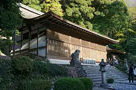 Un bâtiment assez large avec des poutres en bois et des murs peints en blanc. La paroi avant est complètement recouverte par des fenêtres avec grillage en bois.