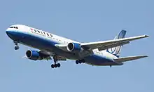 Vue de trois quart d'un avion de ligne biréacteur en vol, avec le train d'atterrissage sorti ; l'avion est peint en bleu et blanc.