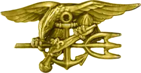 A gold image depicting an eagle perched on an anchor, clutching a trident with one claw and a gun in the other.