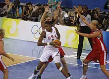 Lisa Leslie de dos par rapport au panier, le ballon dans les mains, avec deux adversaires dans son dos les bras levés.