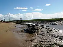 Rive boueuse avec un petit bateau. L'eau peut encore être vue dans le canal vers la droite.