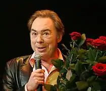 Photographie d'Andrew Lloyd Webber en 2008, un micro à la main et un bouquet de fleurs dans l'autre.