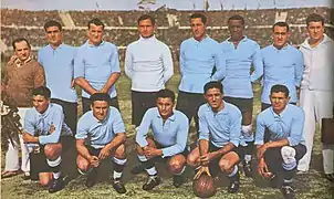 Photo d'avant match d'une équipe de football habillée de bleu, accompagnée de deux officiels, au milieu d'un grand stade.