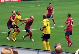 trois footballeurs attendant la retombée du ballon devant le regard de trois autres joueurs