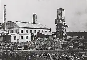 Photo noir et blanc d'une usine avec des charrettes à cheval devant.