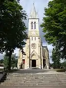 Photographie d'une église vue de face, au clocher-porche carré, surmonté d’une flèche.