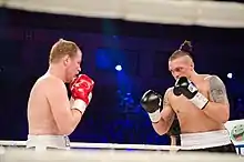 Photographie entre les cordes d'un combat de boxe anglaise lors duquel deux boxeurs se font face.