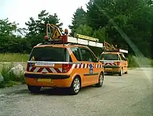 Deux véhicules de service oranges portent du matériel. La mention « arrêts fréquents » figure à l'arrière des deux voitures.