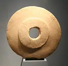 Pierre circulaire d'un jaune ocre avec une large perforation en son centre