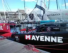 Vue de trois quarts de l'arrière noir du bateau amarré au ponton. Les safrans sont rouges.