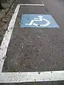 En marquage au sol, signalant une place de stationnement réservée aux handicapés.