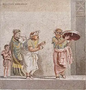 Quatre personnages, de gauche à droite : un nain, une femme avec une double flûte, une femme âgée avec de petits timbales, et une femme âgée qui danse avec un tabourin