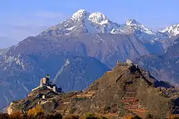 Deux collines sur lesquels reposent à gauche une église fortifiée et à droite un château. En arrière-plan se trouve une montagne enneigée.