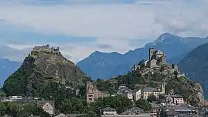 Deux collines sur lesquels reposent à droite une basilique et à gauche un château. En arrière-plan se trouve des montagnes