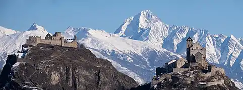 Vue de deux châteaux sur des collines devant des montagnes enneigées.