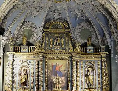 Retable en forme de triptyque. La caisse est ornée d'un tableau peint, les volets latéraux bordés de rinceaux abritent des statues de saints dans des niches à coquilles.
