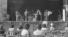 Photo en noir et blanc d'un groupe de rock sur scène prise depuis le public