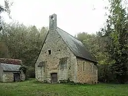 Photographie en couleurs d'un petit édifice religieux sur une pelouse entouré de bois.