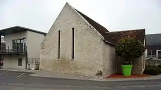 Photographie en couleurs d'un bâtiment sans étage, avec un haut pignon et deux baies étroites et hautes.