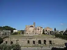 Vue de face depuis le Colisée : la terrasse, les colonnes du péristyle et l'abside à caissons. Au fond à gauche, l'arc de Titus.
