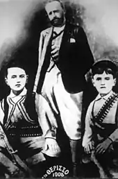 Photographie noir et blanc : un homme barbu, deux garçons à ses pieds.