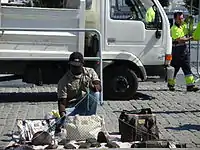 Vendeur de rue à Barcelone, sa marchandise sur une toile tenue par une corde permettant une installation et un départ rapides.