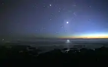 Photographie de nuit d'un océan. On observe de nombreuses étoiles dans le ciel, dont Vénus au centre, bien plus brillante et se reflétant sur l'eau.