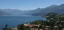 Panorama d'un lac de couleur bleu azur, bordé par les montagnes. On distingue une ville dans la forêt qui borde le lac.