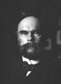 Photographie noir et blanc d'un homme chauve et barbu, de face.