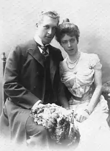 Albert et Élisabeth posent assis une gerbe de fleurs sur les genoux