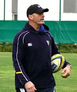 Photographie du haut du corps d'un homme dirigeant un entrainement, une casquette sur la tête, en tenue du club.