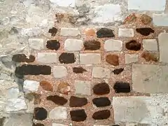 Photographie en couleurs d'un mur dont les pierres dessinent des motifs géométriques.