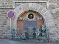 Les vestiges de l'ancienne église en face de la salle des fêtes avec son plan gravé sur la plaque noire. La crypte se trouve derrière le mur en brique.