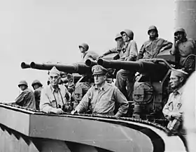 Photo noir et blanc montrant des marins portant des casques militaires et se tenant à porté de canons antiaériens. Deux officiers américaines se penchent sur la rampe du navire et regardant au loin.