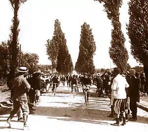 Photographie en noir et blanc d'un groupe de cyclistes fendant la foule attroupée le long d'une route.