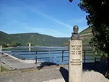 Photographie montrant le buste de Victor Hugo au bord du Rhin viticole (vignoble en arrière-plan à droite).