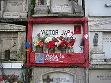 Photo d'un mur découpé en concessions, au centre une tombe peinte en rouge vif avec des fleurs
