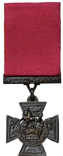 Une croix pattée en bronze suspendue à un ruban cramoisi.