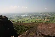 Au premier plan, rochers sombres. En contre-bas vaste panorama d'une large vallée